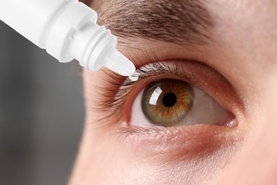 Image of Man applying eye drops on grey background, closeup