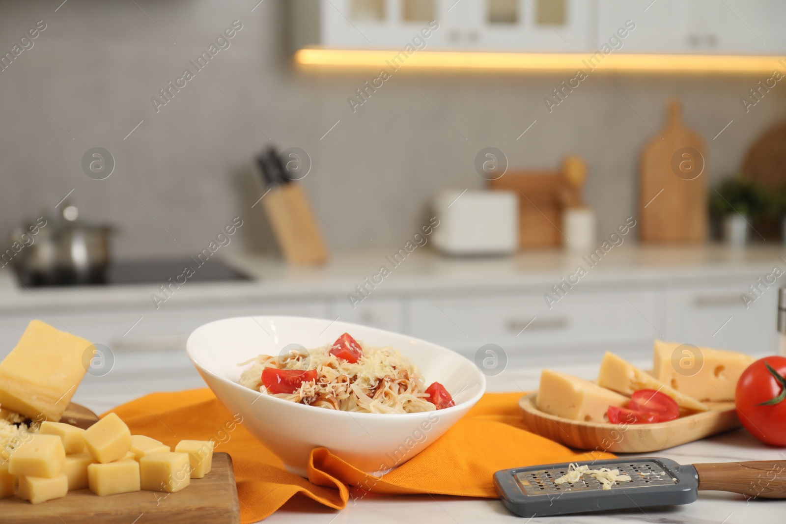 Photo of Delicious pasta with grated cheese and tomatoes on white table in kitchen