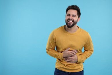 Photo of Handsome young man laughing on light blue background, space for text