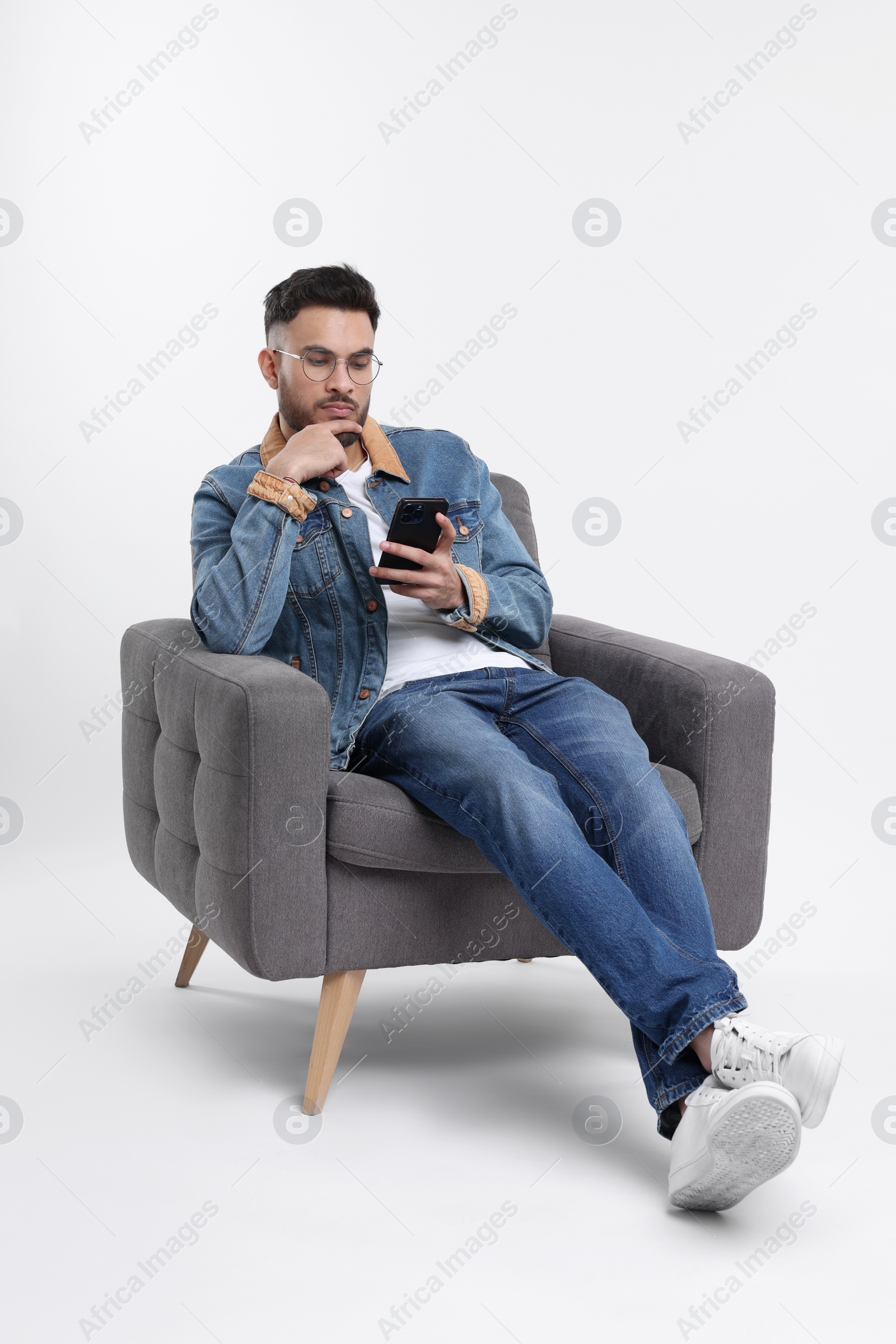 Photo of Handsome man using smartphone in armchair on white background