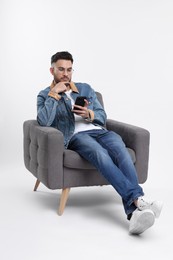 Handsome man using smartphone in armchair on white background