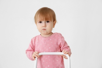 Photo of Cute baby playing with toy walker on light background