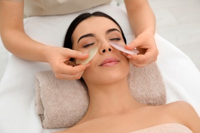 Photo of Young woman receiving facial massage with gua sha tools in beauty salon