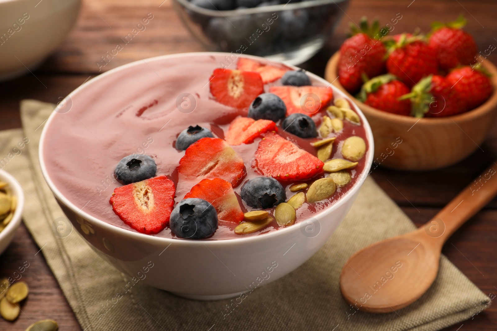 Photo of Bowl of delicious smoothie with fresh blueberries, strawberries and pumpkin seeds on wooden table, closeup