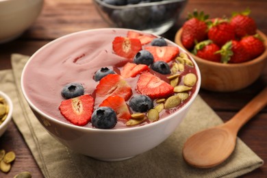 Photo of Bowl of delicious smoothie with fresh blueberries, strawberries and pumpkin seeds on wooden table, closeup