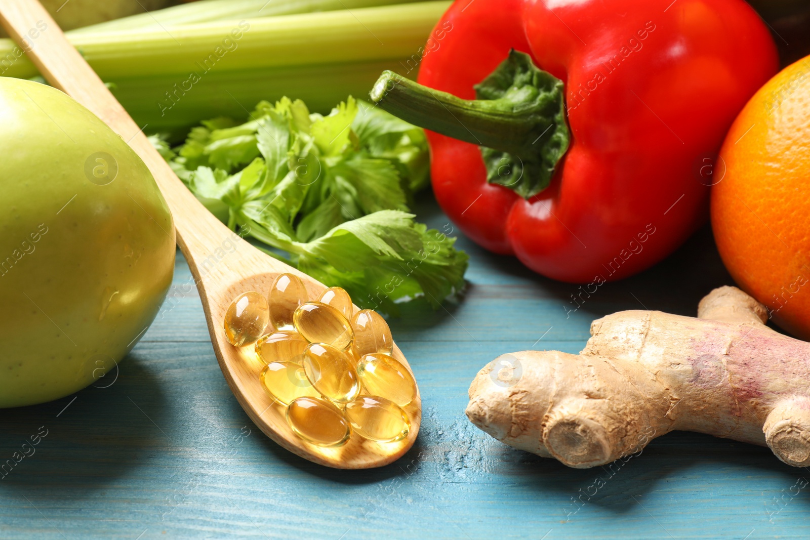 Photo of Dietary supplements. Spoon with capsules near food products on light blue wooden table