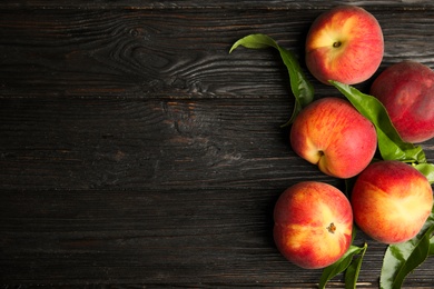 Fresh peaches and leaves on black wooden table, flat lay. Space for text