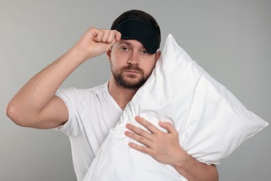 Photo of Sleepy man with pillow and mask on grey background. Insomnia problem
