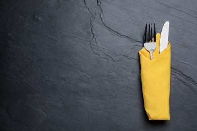 Photo of Shiny fork and knife with napkin on black table, top view. Space for text