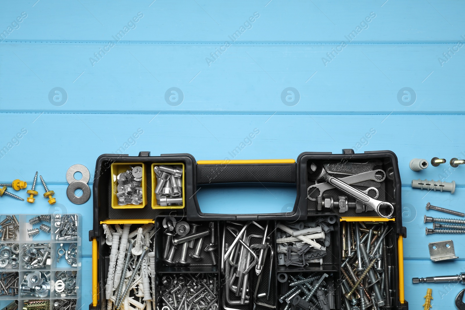 Photo of Organizers with many different fasteners and wrenches on light blue wooden table, flat lay. Space for text