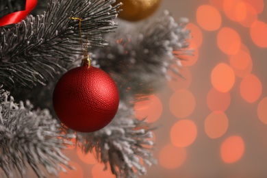 Red holiday bauble hanging on Christmas tree against blurred festive lights, closeup. Space for text