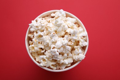 Paper bucket with delicious popcorn on red background, flat lay