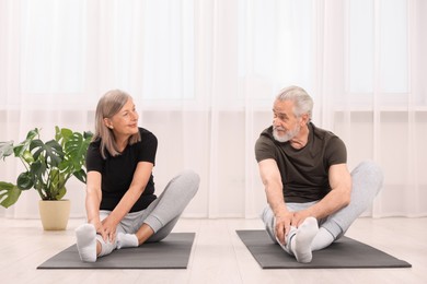 Photo of Senior couple practicing yoga on mats at home