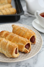 Photo of Delicious sausage rolls and hot drink on white marble table, closeup