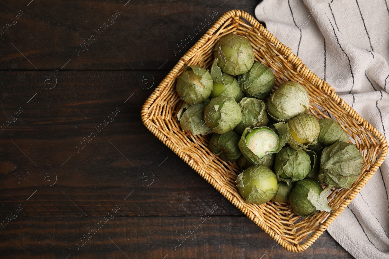 Photo of Fresh green tomatillos with husk in wicker basket on wooden table, top view. Space for text