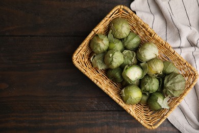 Photo of Fresh green tomatillos with husk in wicker basket on wooden table, top view. Space for text