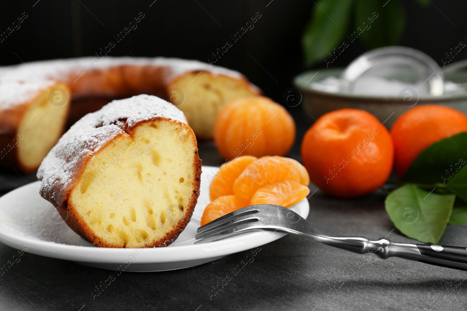 Photo of Piece of delicious homemade yogurt cake with powdered sugar and tangerines on gray table