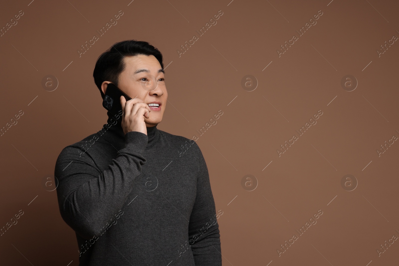 Photo of Portrait of happy man with smartphone on brown background. Space for text