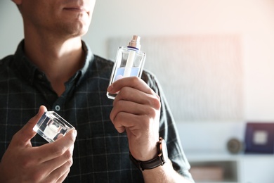 Young man with bottle of perfume indoors, closeup. Space for text