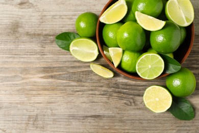 Photo of Tasty ripe limes in bowl on wooden table, top view