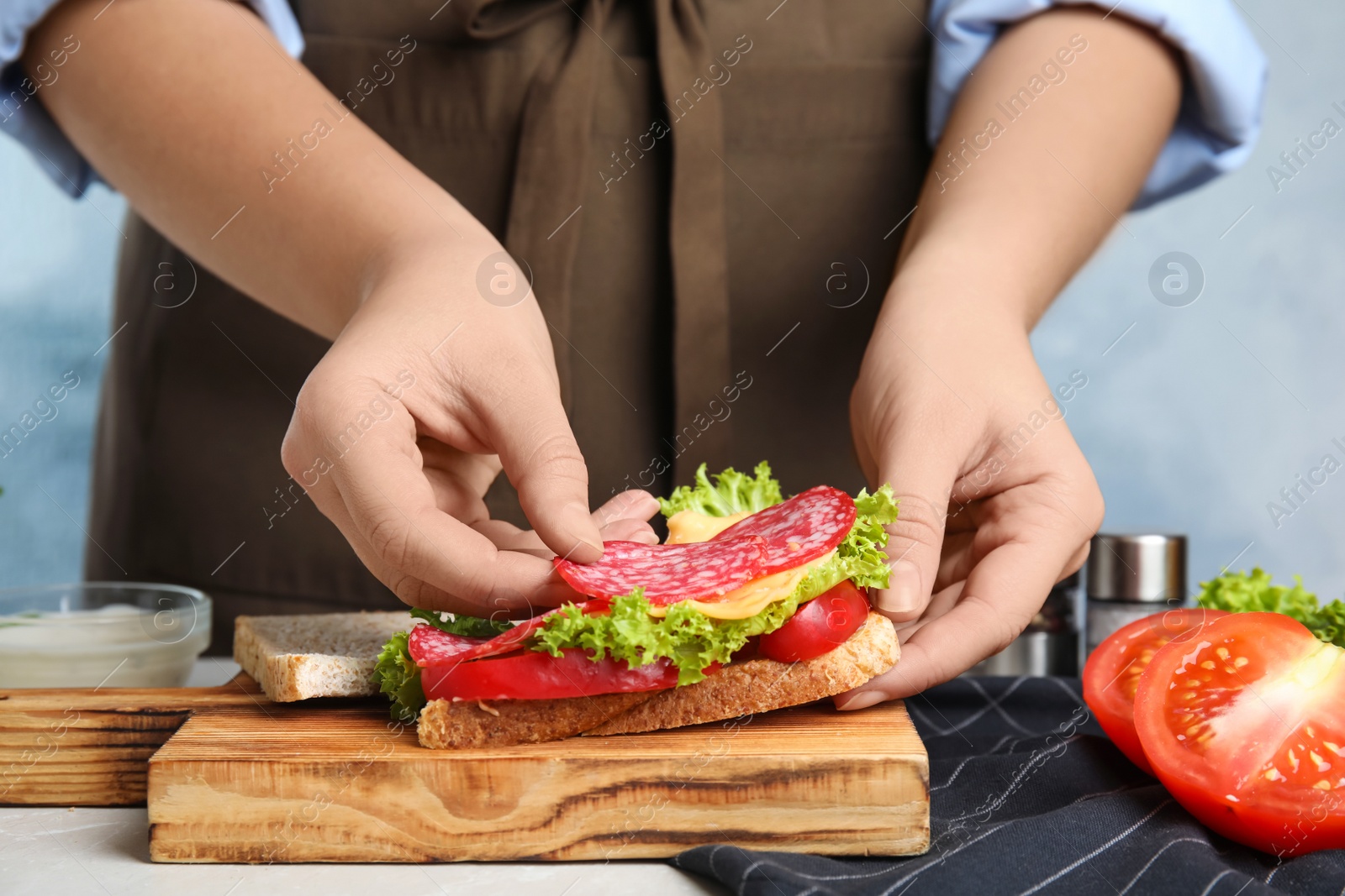 Photo of Woman making tasty sandwich with sausage at table, closeup