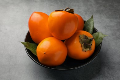 Delicious ripe persimmons in bowl on light gray table