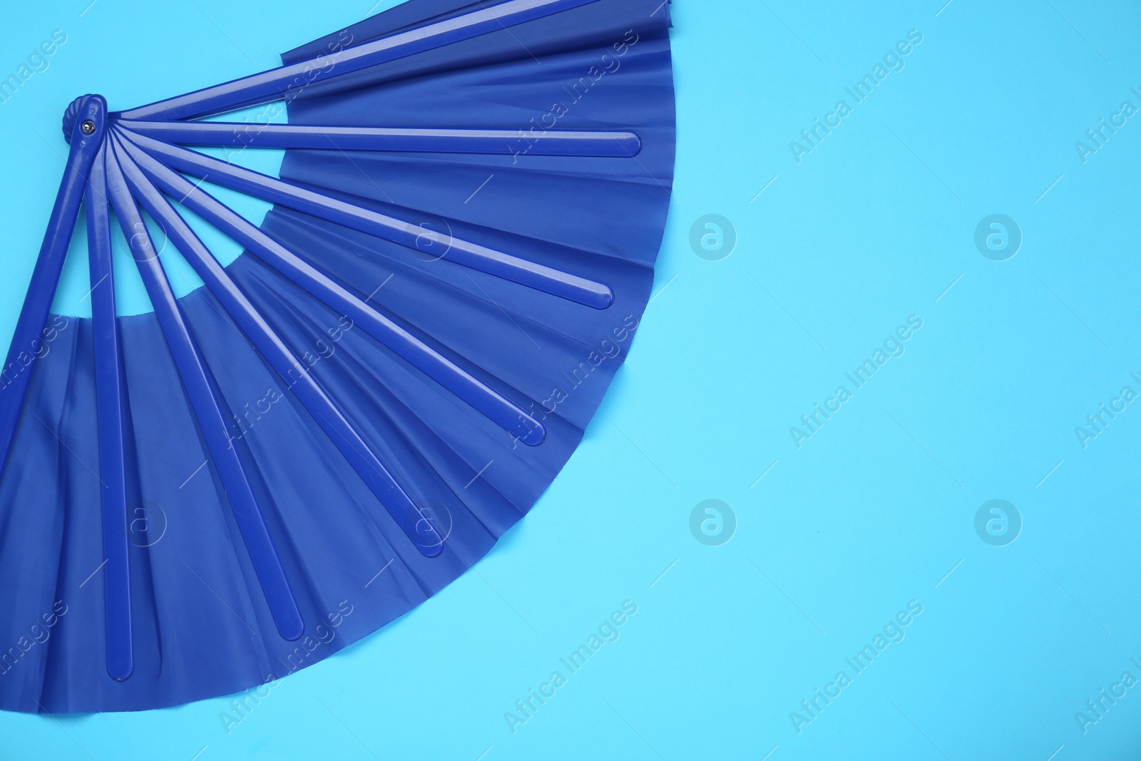 Photo of Bright color hand fan on light blue background, top view. Space for text