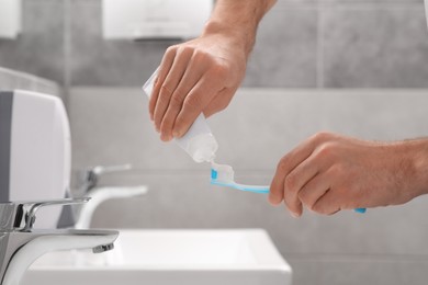 Photo of Man squeezing toothpaste from tube onto toothbrush in bathroom, closeup