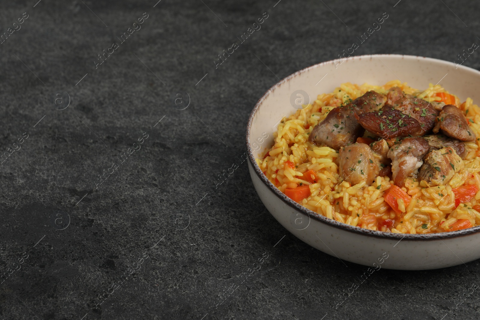 Photo of Delicious pilaf with meat on grey textured table, space for text