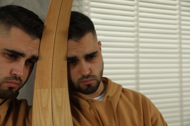 Sad young man near mirror at home