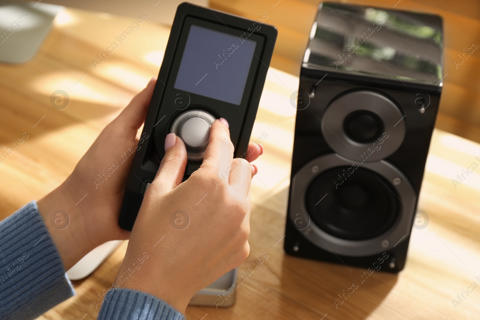 Photo of Woman using remote to control audio speakers at wooden table indoors, closeup