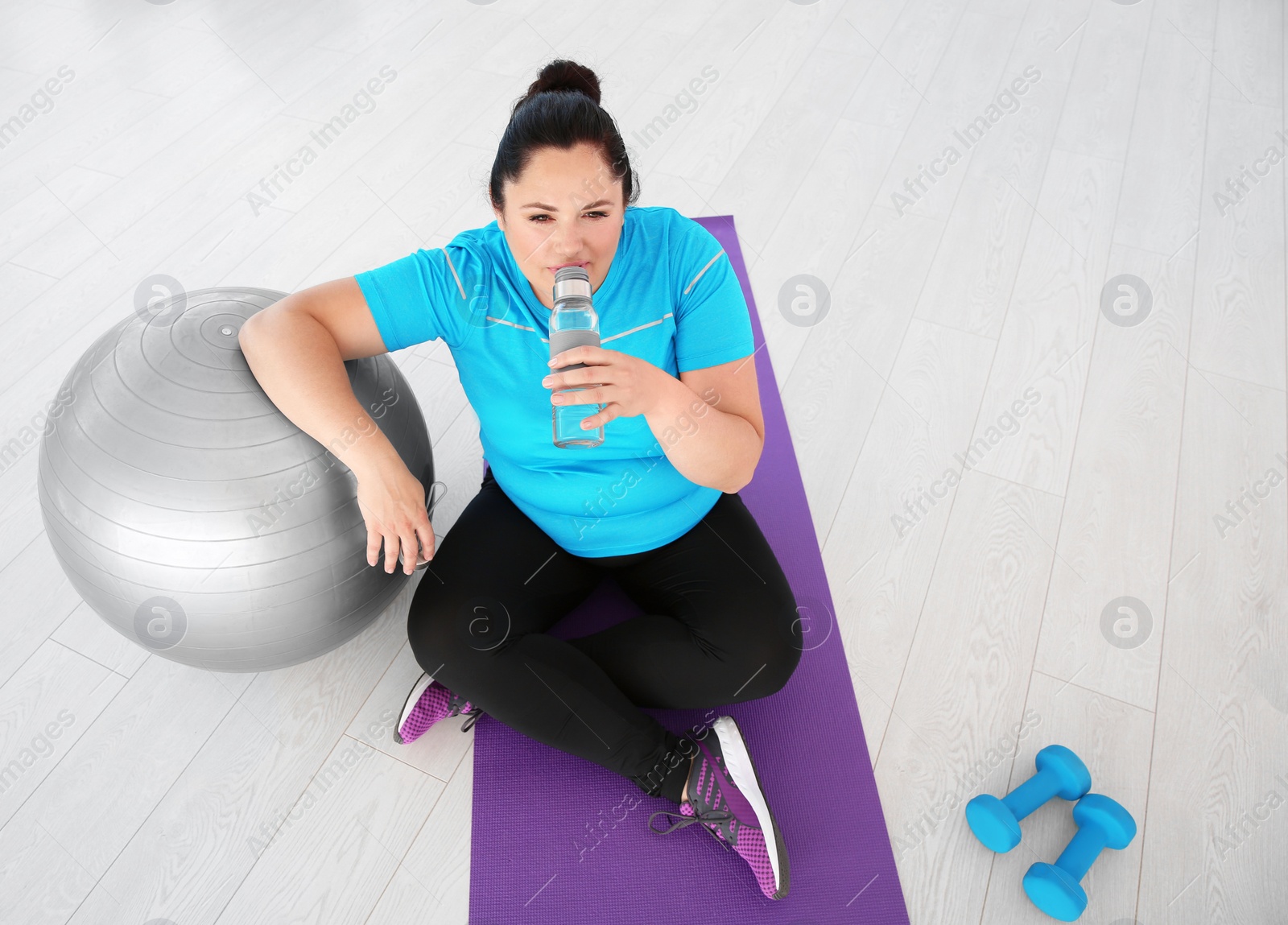 Photo of Tired overweight woman drinking water in gym