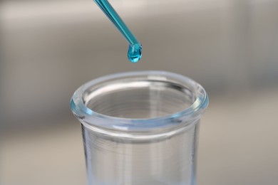 Photo of Laboratory analysis. Dripping blue liquid into flask on blurred background, closeup