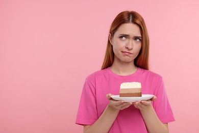 Photo of Unhappy young woman with piece of tasty cake on pink background, space for text