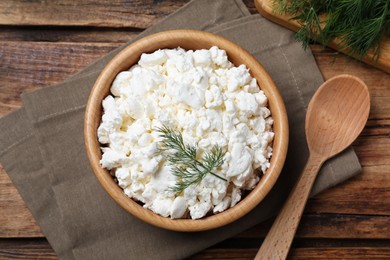 Photo of Fresh cottage cheese with dill in wooden bowl and spoon on table, flat lay