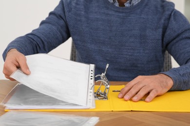 Businessman putting document into file folder at wooden table in office, closeup