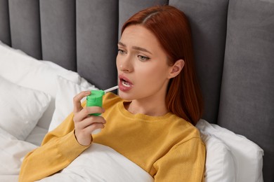 Photo of Young woman using throat spray in bed