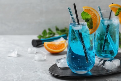 Photo of Glass of delicious Blue Lagoon cocktail with ice on light table. Space for text