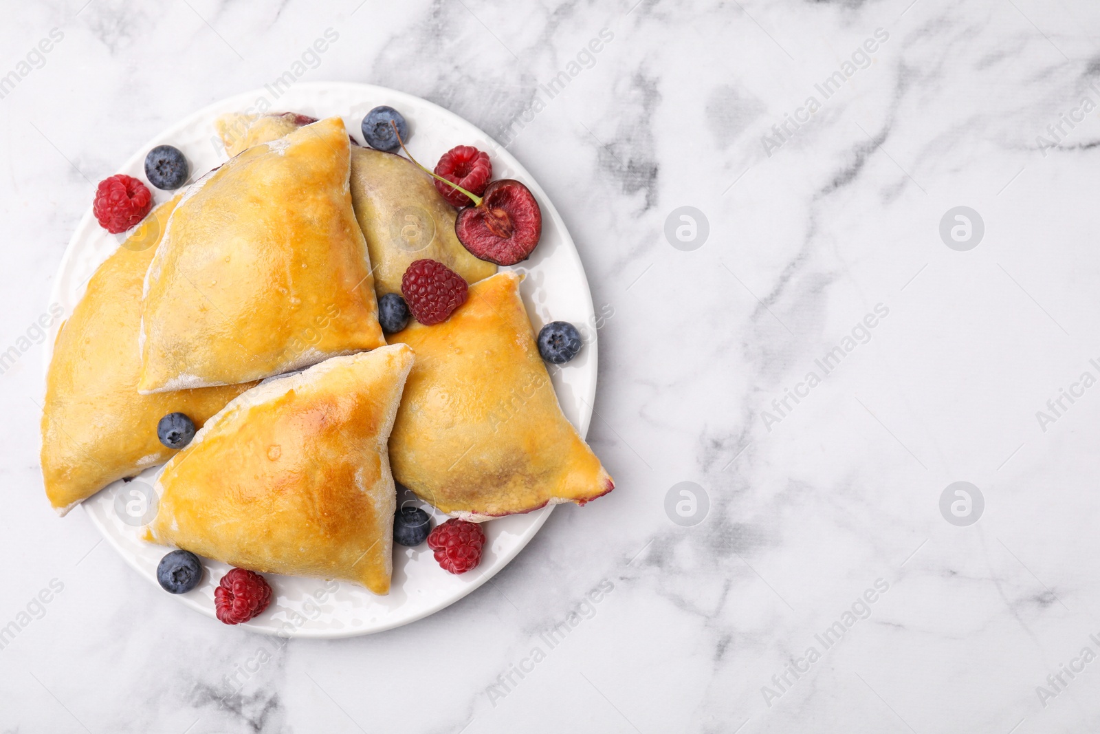 Photo of Delicious samosas with cherry and berries on white marble table, top view. Space for text