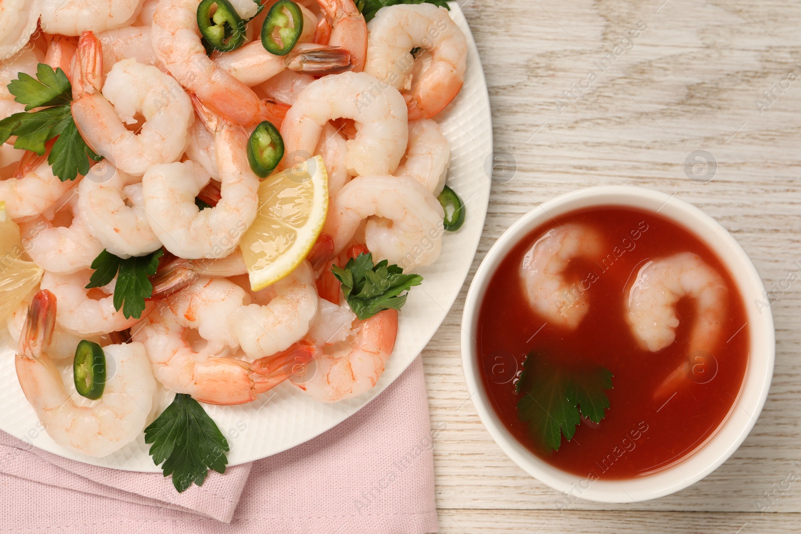 Photo of Tasty boiled shrimps with cocktail sauce, chili, parsley and lemon on light wooden table, flat lay