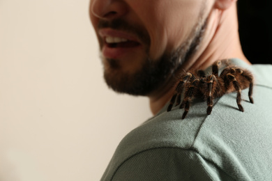 Scared man with tarantula on beige background, closeup. Arachnophobia (fear of spiders)