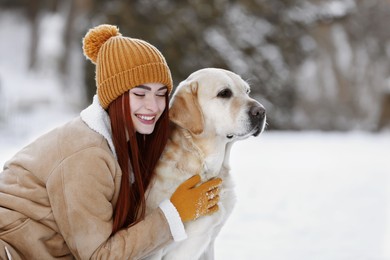 Beautiful young woman hugging cute Labrador Retriever on winter day outdoors