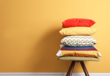 Photo of Many different pillows on chair near color wall with space for text