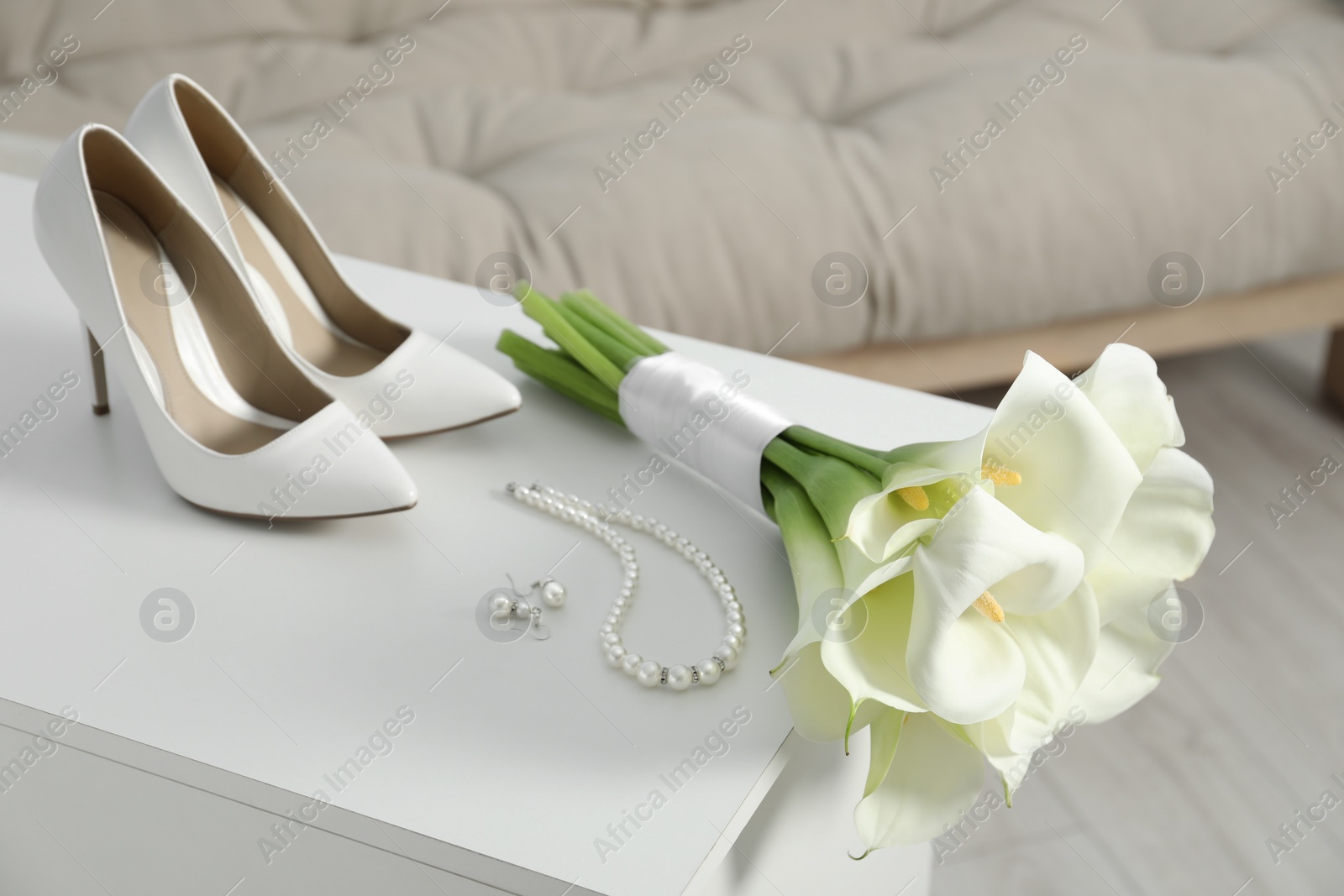 Photo of Beautiful calla lily flowers tied with ribbon, shoes and jewelry on white chest of drawers indoors