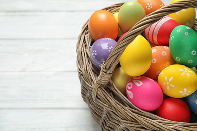 Photo of Colorful Easter eggs in basket on white wooden table, closeup. Space for text