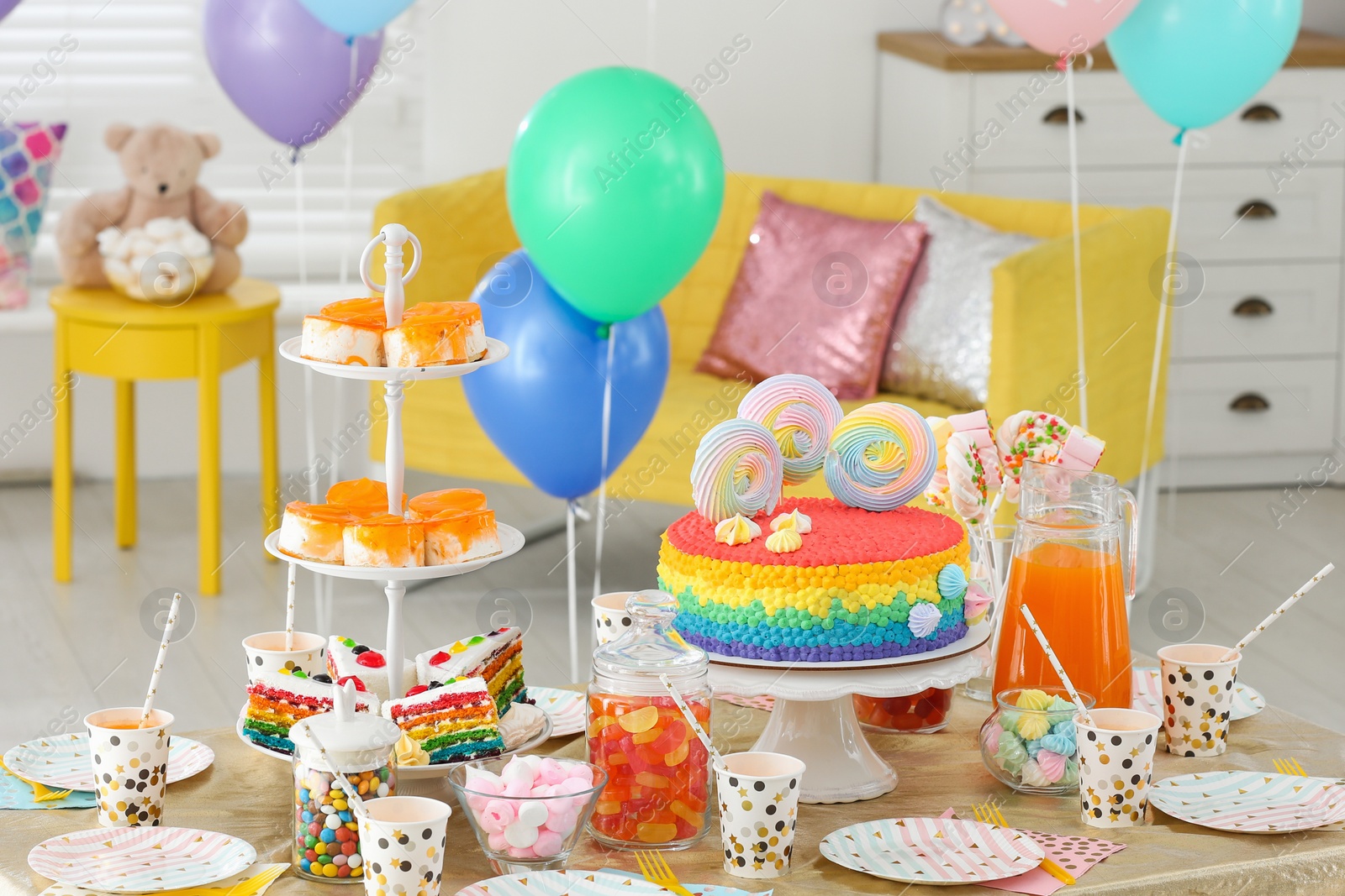 Photo of Bright birthday cake and other treats on table in decorated room