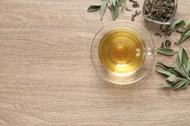 Photo of Cup of aromatic sage tea, dry and fresh leaves on wooden table, flat lay. Space for text