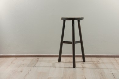 Photo of Stylish wooden stool near light wall indoors. Space for text