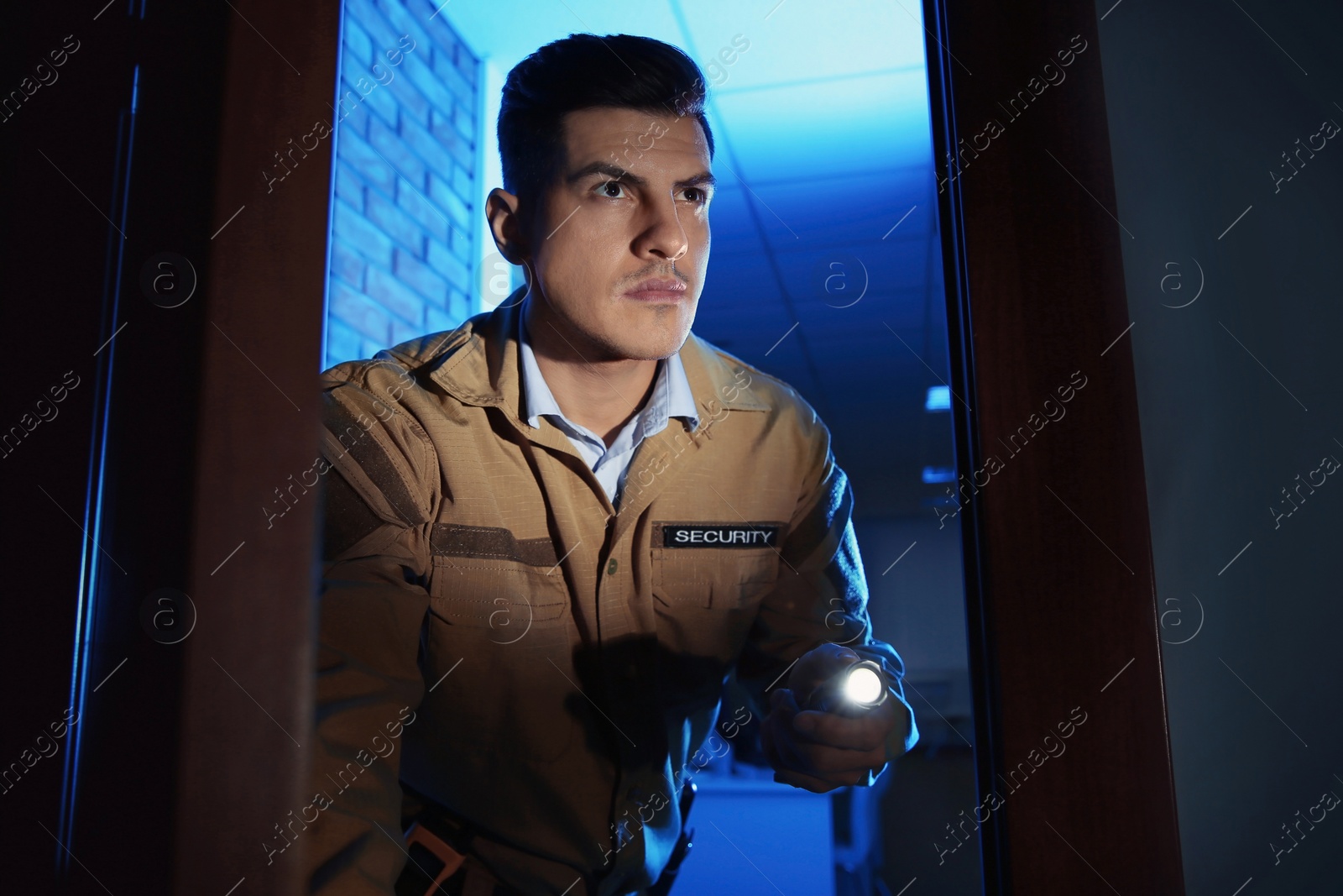 Photo of Professional security guard with flashlight checking dark room