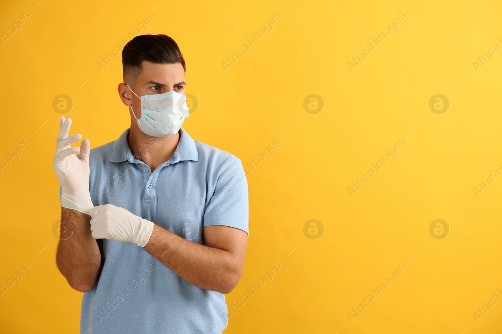Photo of Man in protective face mask putting on medical gloves against yellow background. Space for text
